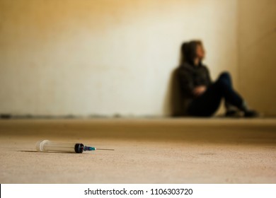 Drug addicted teen sitting on the cement floor with syringe in front of. Anti drug concept
