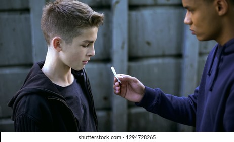 Drug dealer boy treating younger friend with marijuana cigarette, addiction