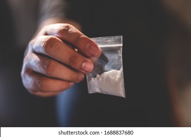 Drug dealer selling junkie. Man hand holds plastic packet or bag with addict narcotics  cocaine powder or another, drug dealer sale and danger addiction overdose concept.