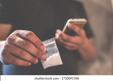 Drug Dealer Selling. Man Hand Hold Use Mobile Smart Phone Contact Junkie. Plastic Packet Or Bag With Addict Narcotics  Cocaine Powder Or Another, Drug Dealer Sale And Danger Addiction Overdose Concept