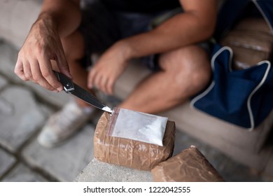 Drug Dealer Testing Heroin Purity And Preparing Goods For Trafficking, Packing Cocaine Bricks, Pills And Marijuana. Focus On The Tip Of The Knife