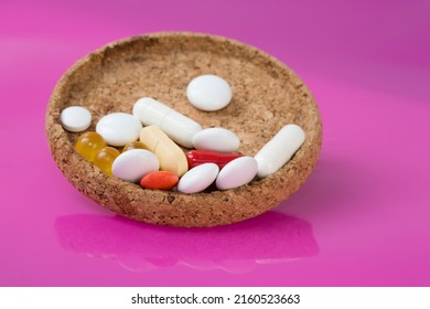 Drug Interaction Concept. Drug Cocktail Including Medicinal Products, Vitamins, Minerals, Herbs On Small Cork Plate On Pink Background