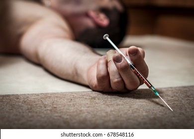 Drug overdose and opioid epidemic concept with man lying naked on the floor in the home kitchen after overdosing on opioid drugs and holding a syringe with heroin or possibly other narcotic substance