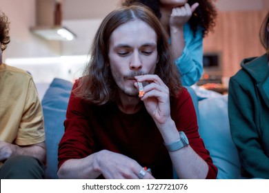 Drug User. Young Hipster Guy Smoking Cannabis Marijuana Cigarette Or Joint While Relaxing With Friends On The Couch At Home. Young People Smoking Marijuana Together. Marijuana, Weed Legalization