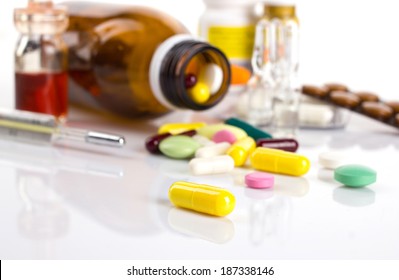 drug in yellow capsule on white table and blurred background with different medicament in blisters and bottle and thermometer - Shutterstock ID 187338146