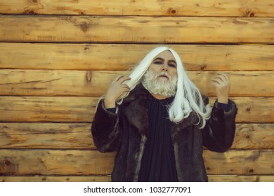 Druid old man with long grey hair and beard on serious face outdoor on wooden background in fur coat