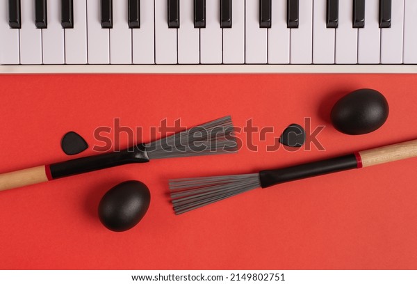 Drum brushes, shakers,\
midi keyboard and guitar picks on a bright red background. Top\
view, flat lay. 