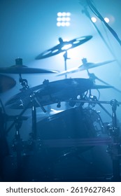 Drum kit in atmospheric stage lighting. Drum cymbals illuminated by dim light, wrapped with smoke.