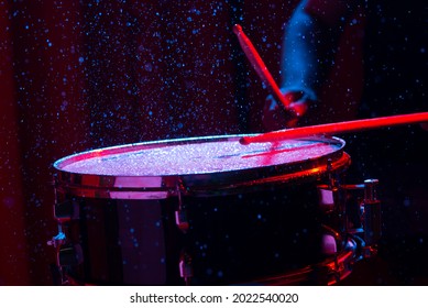 Drum sticks hitting snare drum with splashing water on dark background with red and blue  studio lighting. Dynamic scene.