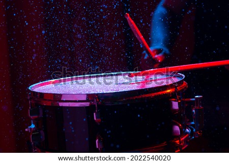 Drum sticks hitting snare drum with splashing water on dark background with red and blue  studio lighting. Dynamic scene.