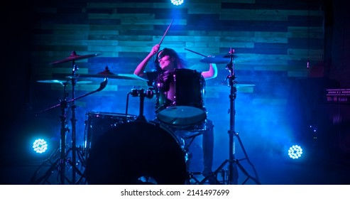 Drummer girl energetically playing the drums in blue and red twinkling strobe lights on stage during show. Drummer girl concert concept. Camera is getting closer to the drummer girl.