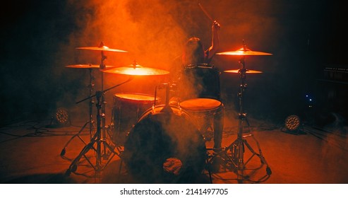Drummer girl plays the drums in shimmering orange beam. The girl finishes the performance on the nightclub stage, makes the last hit on the cymbal