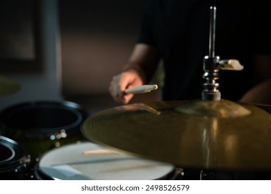 The drummer hits the hi-hat with a drumstick, making a loud, sonorous sound. The drummer is wearing a black shirt, and the cymbal is large and golden. The camera is aimed at the plate in close-up - Powered by Shutterstock