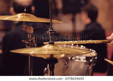 A drummer performing on a drum set, striking the drums and cymbals with sticks.