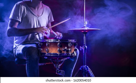 A drummer plays drums on a blue background. Beautiful special effects of light and smoke. The process of playing a musical instrument. The concept of music. Close-up photo.