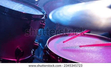 A drummer plays on a dark stage in the fog and neon lights.