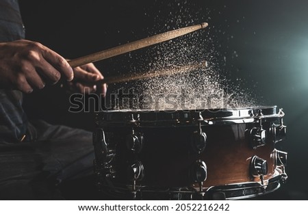 Drummer using drum sticks hitting snare drum with splashing water on black background under studio lighting close up.