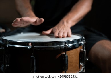 A drummer's hand strikes a snare drum, creating a sharp and distinct sound. The drum is wooden with chrome hardware, and the hand is well-defined