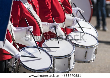 Drummers in red uniforms on a row at a spring parade with white gloves drumming on drums