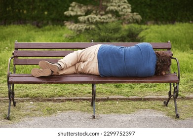 Drunk adult man, drunkard, alcoholic sleeps in the park outdoors on a wooden bench. Photography, portrait, lifestyle.