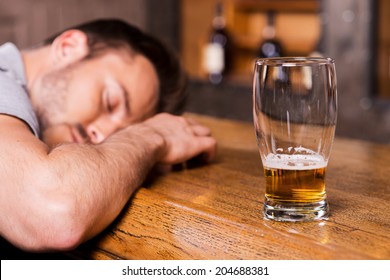 Drunk again. Drunk male customer leaning at the bar counter and sleeping while glass with beer standing near him 