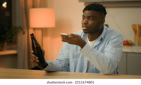 Drunk alcoholism addicted African American ethnic man biracial guy male drinking alcohol drink beer at home kitchen talking mobile phone call loudspeaker record audio voice message voicemail cellphone - Powered by Shutterstock