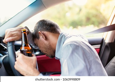 Drunk asian young man drives a car with a bottle of beer with sunset background, Dangerous driving concept