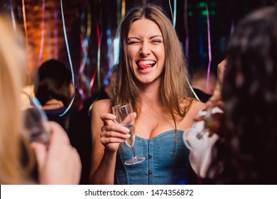 Drunk brown hair woman or girl hold wineglass champagne squint wink and show tongue on party celebration toast friends girls people blonde and brunette confetti loft interior brick wall background