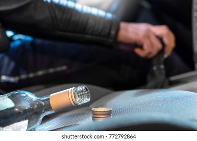 Drunk Driving Concept. Young Man Driving Car Under The Influence Of Alcohol. Hand On Gear Stick. Close Up Of Empty Bottle Of Wine On Front Seat. Traffic Safety Risk.