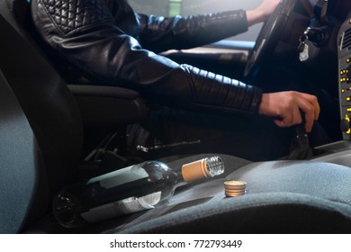 Drunk driving concept. Young man driving car under the influence of alcohol. Empty bottle of wine on front seat. Going away from party late at night. Traffic safety risk.