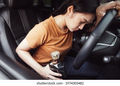 Drunk female driver in car, Bottle of alcohol in a woman's hand behind the steering wheel - a concept of driving intoxicated