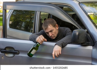 Drunk And Irresponsible Driver Hanging On The Doors Of His Car With A Bottle Of Alcoholic Beverage