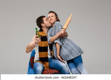 Drunk Man Kissing Displeased Wife, Holding Beer Over Grey Background.