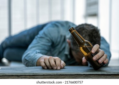 DRUNK MAN LYING ON THE FLOOR ASLEEP WITH A BOTTLE OF BEER IN HIS HAND. ALCOHOL CONSUMPTION ADDICTION. ALCOHOLISM CONCEPT. FOCUS SELECTED. - Shutterstock ID 2176600757
