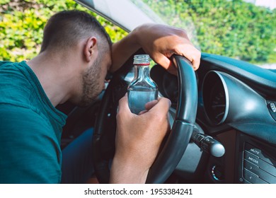Drunk man sleeping on the steering wheel in his car with a bottle of vodka in his hands. Drunk driver - Shutterstock ID 1953384241