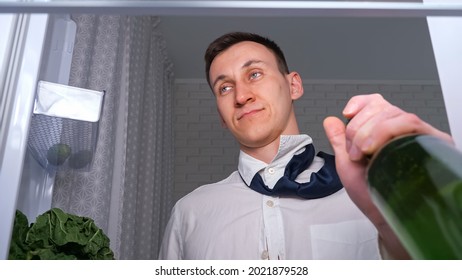 Drunk Man In White Shirt And Tie Opens Door To Takes Bottle Of Cold Beer From Shelf In Dark Kitchen, Close View From Inside New Refrigerator