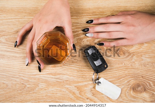 drunk woman holding a glass of whiskey and car keys\
on the table