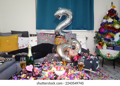 drunk woman lying on sofa after celebrating end of 2022. new year 2023. january 1. colorful confetti and big number balloons. silvester party. sleeping girl