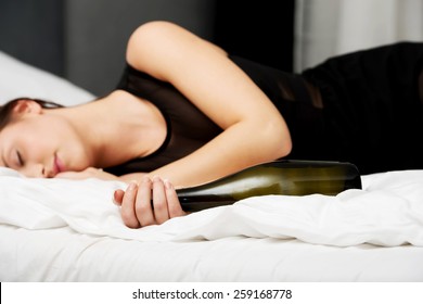 Drunk woman sleeping on bed with bottle of wine.