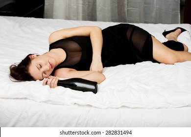 Drunk woman sleeping on bed with bottle of wine.
