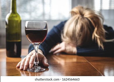 Drunk Woman Sleeping On Table After Drinking Wine. Alcohol Addiction Concept. Female Drinking Red Wine At Home Alone. Social Issues