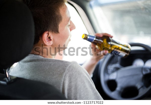Drunk young driver drinking a bottle of alcohol\
during driving the car, campaign picture, do not drink alcohol when\
you drive