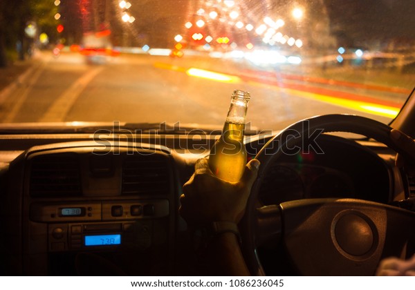 Drunk young man\
drives a car with a bottle of beer. This is a campaign picture of\
\