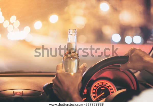 Drunk young man drives a car with a bottle of beer.\
 This is a campaign picture of \