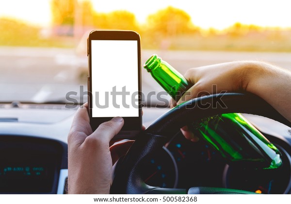 Drunk young man driving a car with a bottle of beer\
and mobile phone. Don\'t drink and drive concept. Don\'t text and\
drive. Driving under the influence (DUI), Driving while intoxicated\
(DWI)