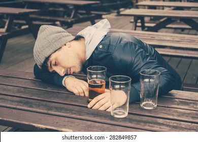 Drunk young man sleeping at pub in London. He is sitting at table outdoor with some empty glasses on the table.