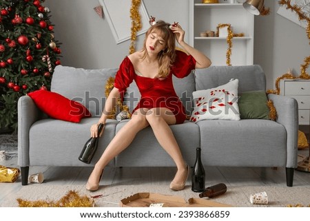 Drunk young woman sitting on sofa in messy living room after New Year party