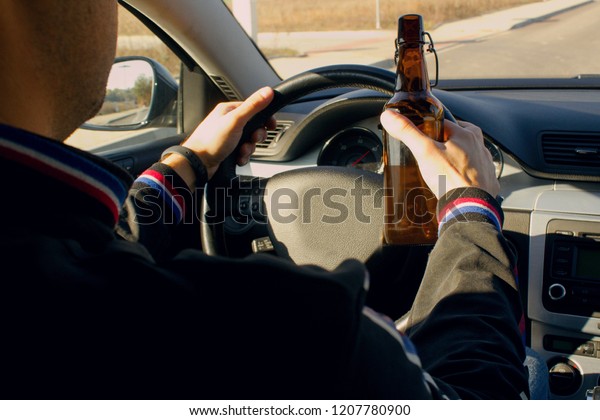 A drunken\
man driving a car with a bottle of alcohol in his hand.A man holds\
a driving wheel and a bottle of\
beer.