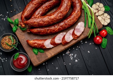 Dry Appetizing Smoked Pork Sausage On A Dark Background With Different Spices And Vegetables. Photo For The Menu