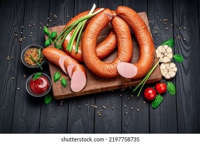 Dry Appetizing Smoked Pork Sausage On A Dark Background With Different Spices And Vegetables. Photo For The Menu